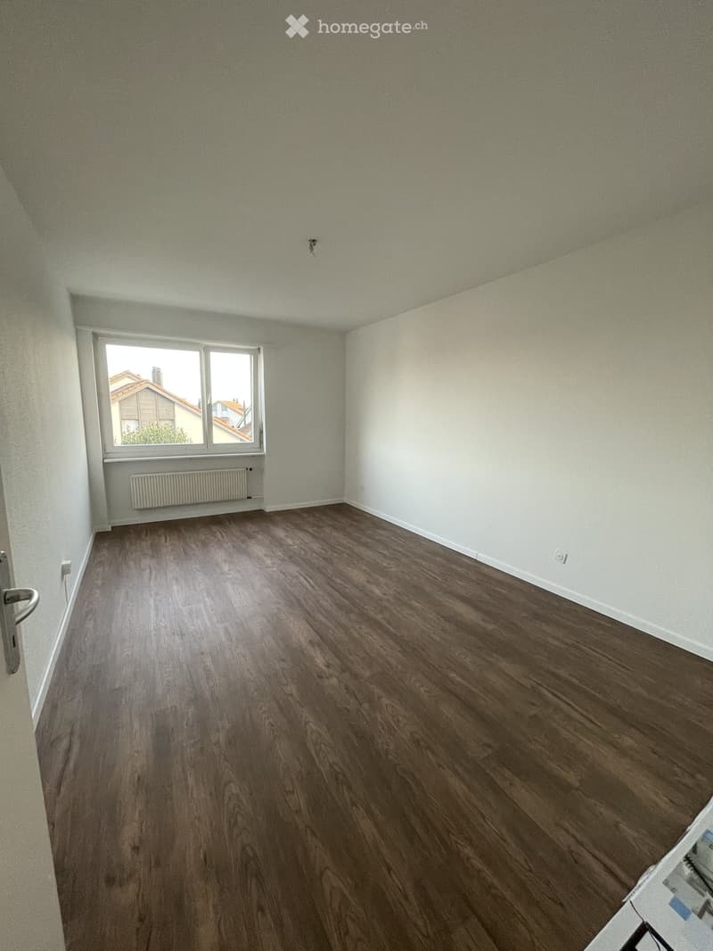 Empty room with wooden flooring, white walls, and a window with a radiator below it.