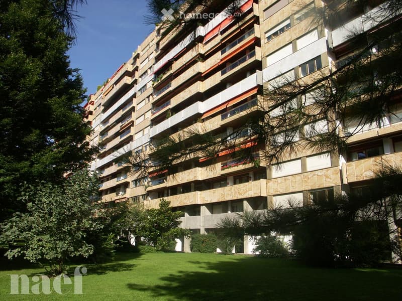 A multi-story residential building with balconies and greenery in the foreground.