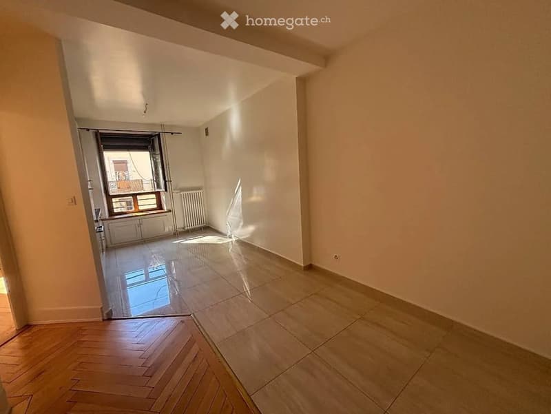 Empty room with light-colored walls, polished wooden floor, and a large window with a view of a balcony. The room is unfurnished and has a clean, minimalist design.