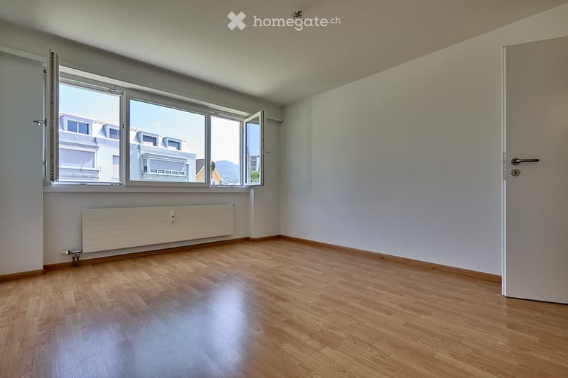 Empty room with wooden flooring, white walls, large windows, and a radiator. No furniture or equipment present.