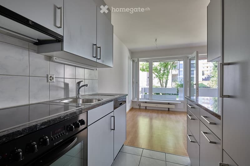 Modern kitchen with white cabinets, stainless steel sink, oven, and wooden flooring.