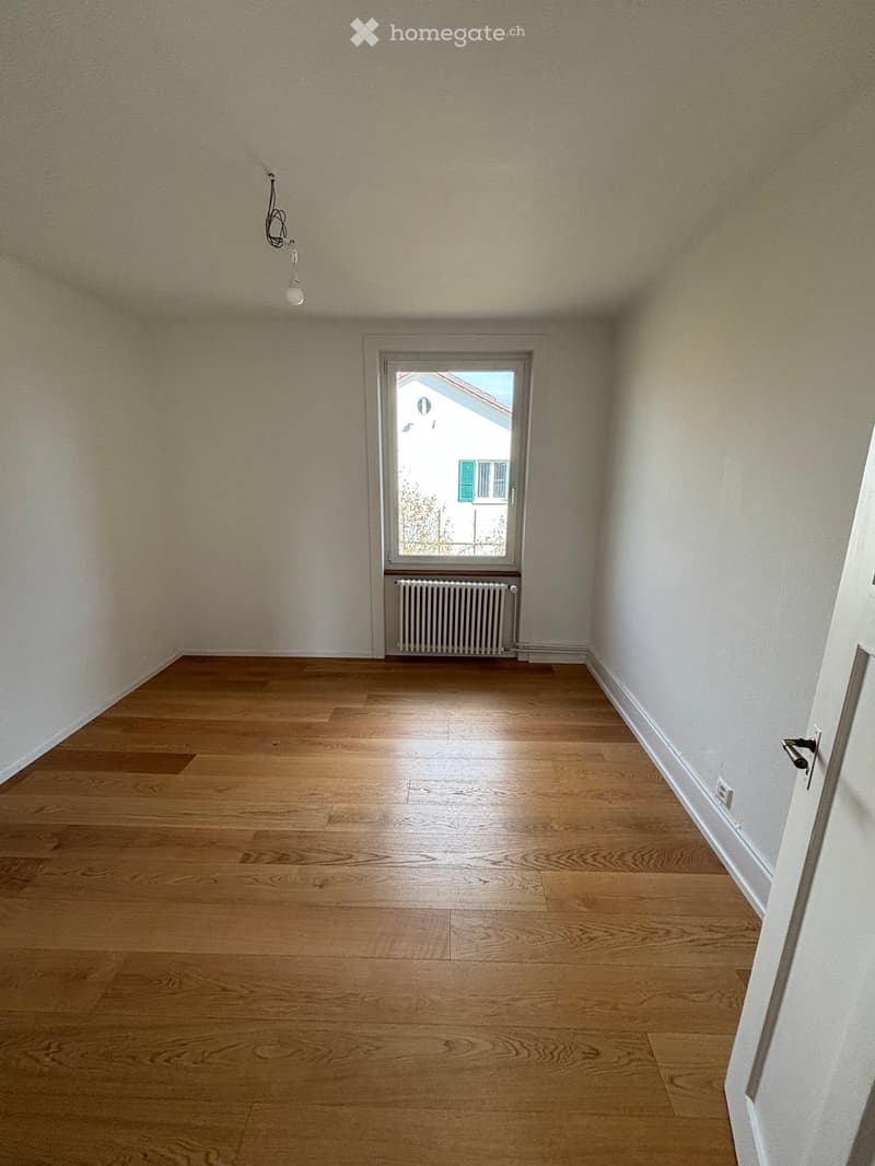 Empty room with wooden flooring, white walls, a window with a radiator below, and a light fixture on the ceiling.