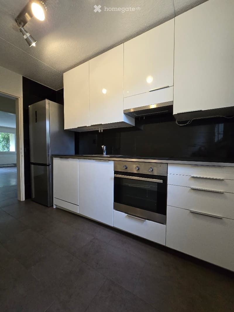 Modern kitchen with white cabinets, stainless steel oven, refrigerator, and dark tiled floor.