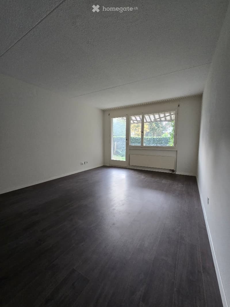 Empty room with dark wooden flooring, white walls, and a large window with blinds. No furniture or equipment present.