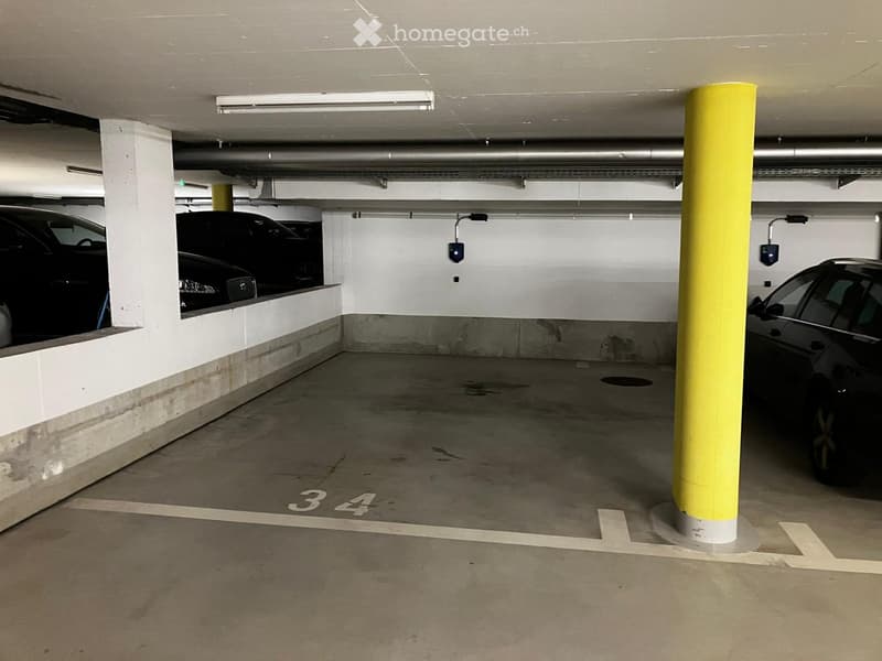 Underground parking area with marked parking spaces, yellow safety pillars, and two parked cars.