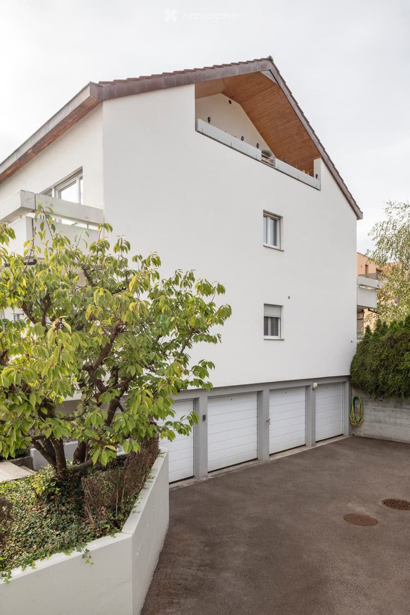 Modern two-story house with white exterior, grey garage doors, and a small tree in the front yard.