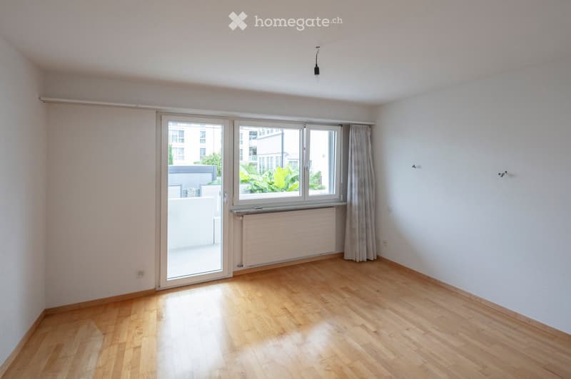 Empty room with wooden flooring, large windows, and a radiator. No furniture or equipment present.