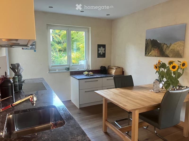 Modern kitchen with a wooden dining table, chairs, stainless steel sink, and various appliances.