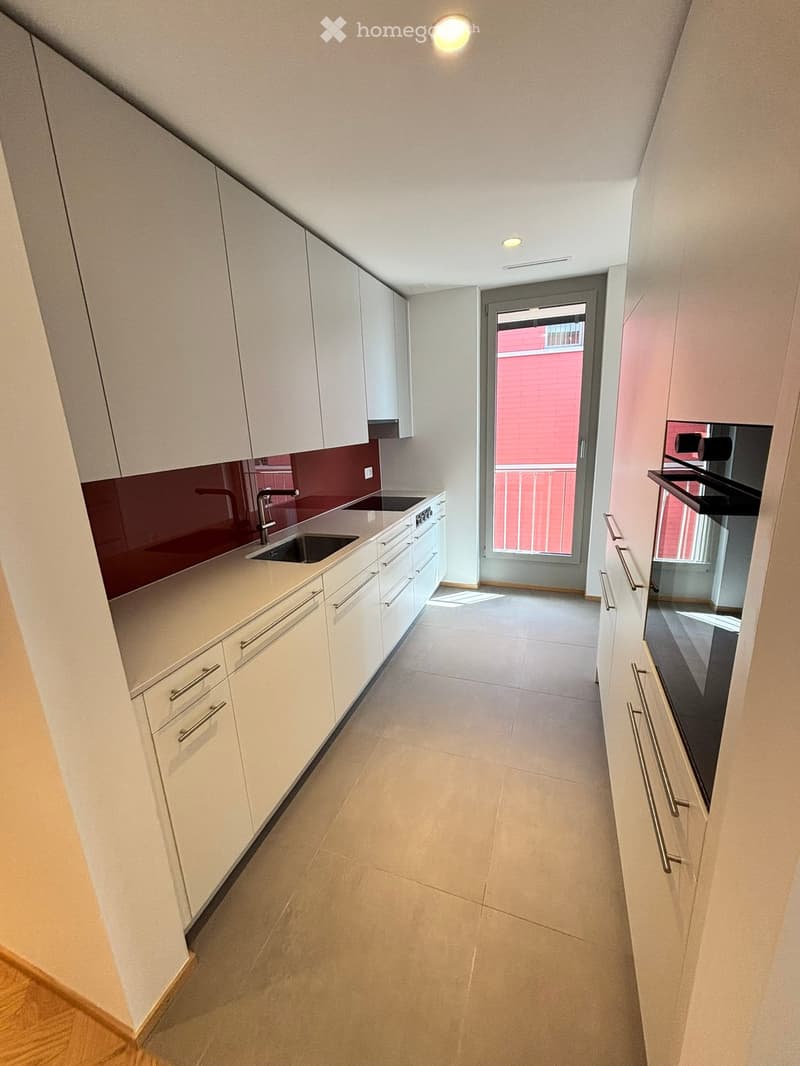 Modern kitchen with white cabinets, a sink, and a red backsplash. The floor is tiled, and there is a doorway leading to a balcony.