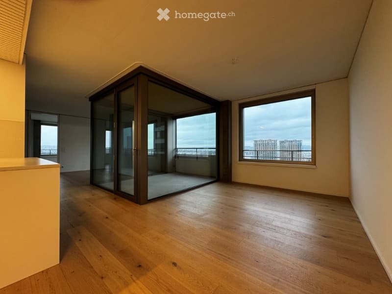Empty room with wooden flooring, large windows, and a sliding glass door leading to a balcony with a city view.