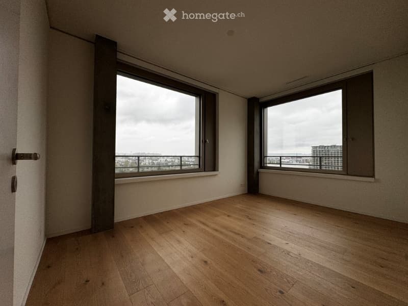 Empty room with wooden flooring, large windows offering a city view, and a door leading to a balcony.