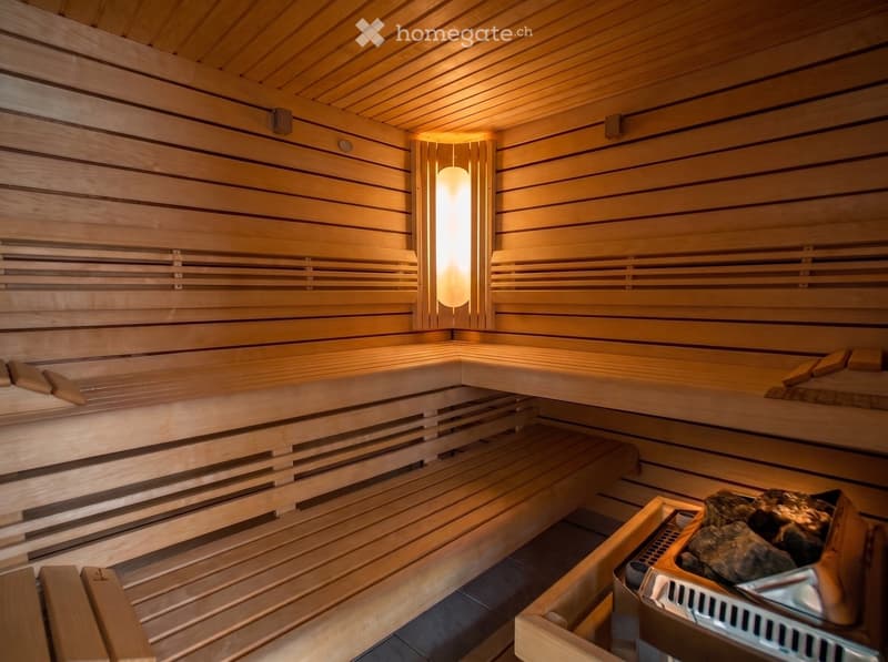 A wooden sauna with multiple benches, a light fixture, and a stone rock pile in the corner.