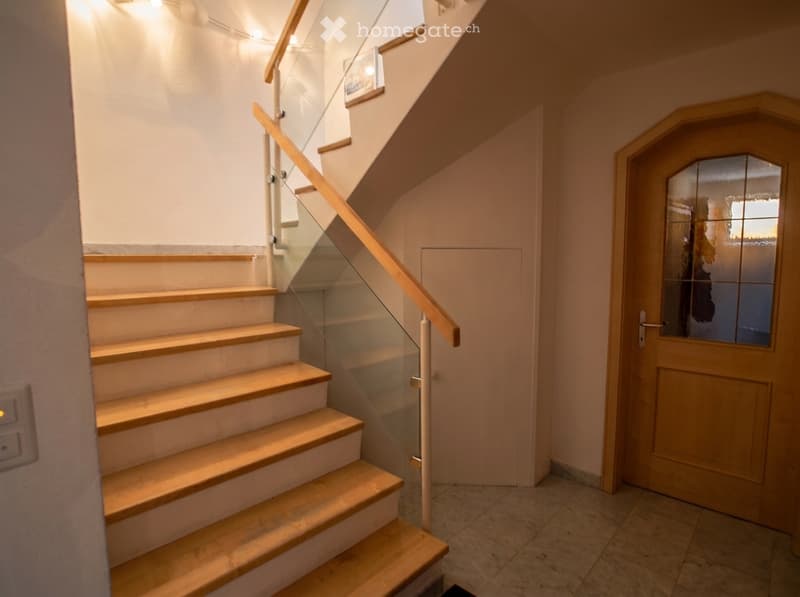 Wooden staircase with glass railing, white walls, and a wooden door with frosted glass panels.