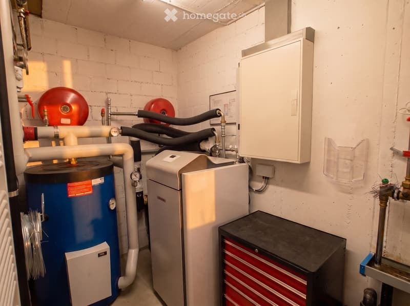 Utility room with water heater, boiler, toolbox, and various pipes and valves.