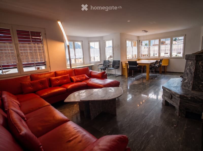 Modern living room with a red leather sectional sofa, coffee table, fireplace, dining area with table and chairs, large windows with blinds, and a tall floor lamp.