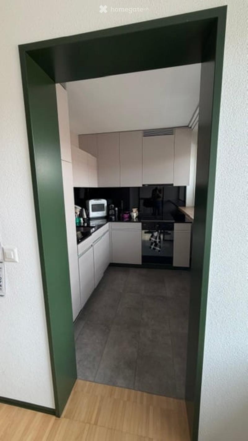 Modern kitchen with white cabinets, black countertops, and stainless steel appliances including a stove and microwave. The space features a dark tiled floor and a visible sink with a faucet.