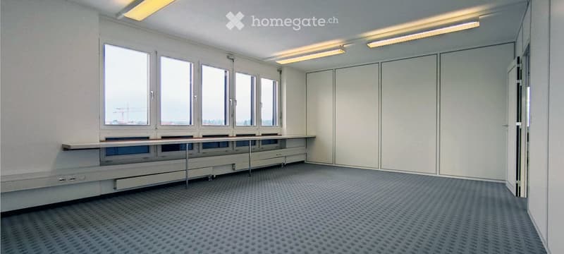 Empty room with large windows, white walls, and a long table with drawers along one wall. No furniture or personal items are present.