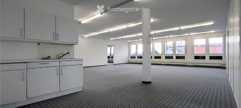 Empty room with white walls, grey carpeted floor, white cabinets, sink, and large windows with blinds.