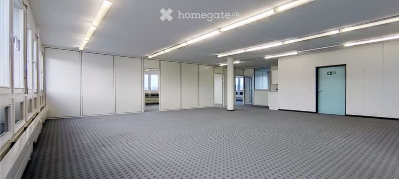 Empty room with white walls, carpeted floor, large windows, and a central column. No furniture or equipment present.