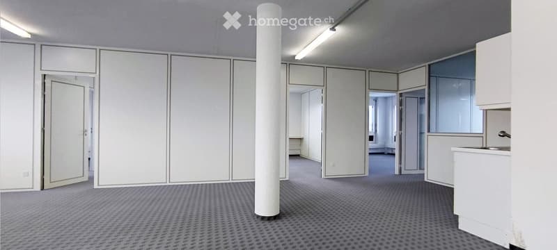 Empty room with white walls, grey carpet, and a central white pillar. No furniture or equipment is present.