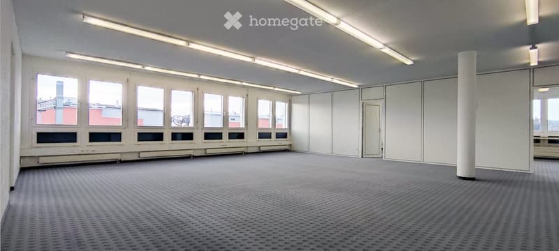 Empty room with bare walls, carpeted floor, large windows, and a central column. No furniture or equipment present.