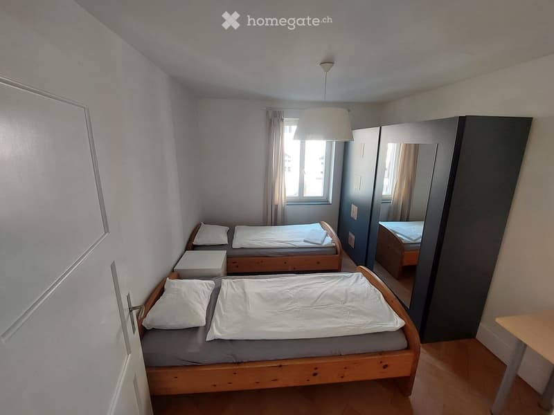 Cozy bedroom with two single beds, nightstand, and a large mirror reflecting the room.