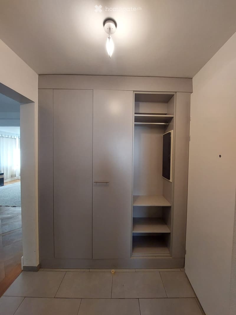 Empty room with grey built-in wardrobes, tiled floor, and a single ceiling light fixture.