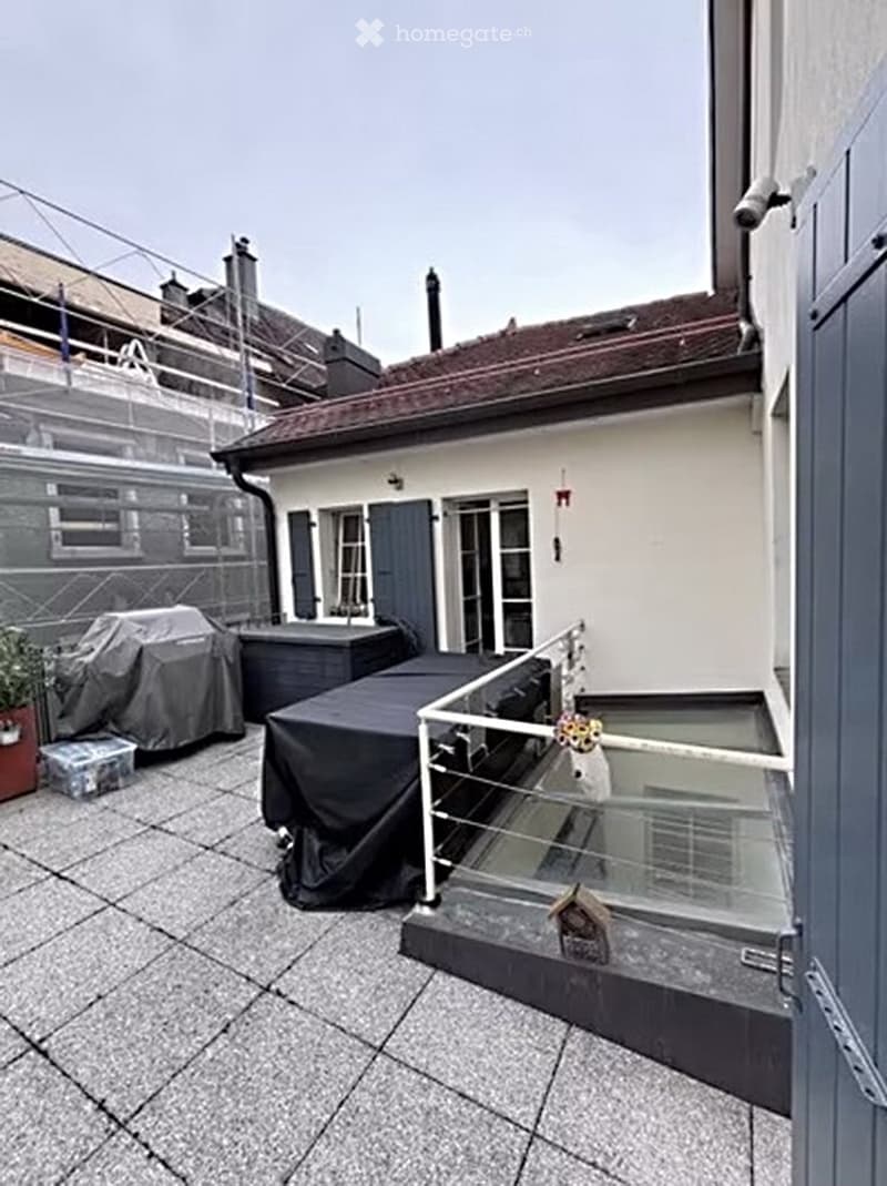 Rooftop terrace with grey tiled flooring, covered furniture, small staircase leading to a lower level, and a view of neighboring buildings.