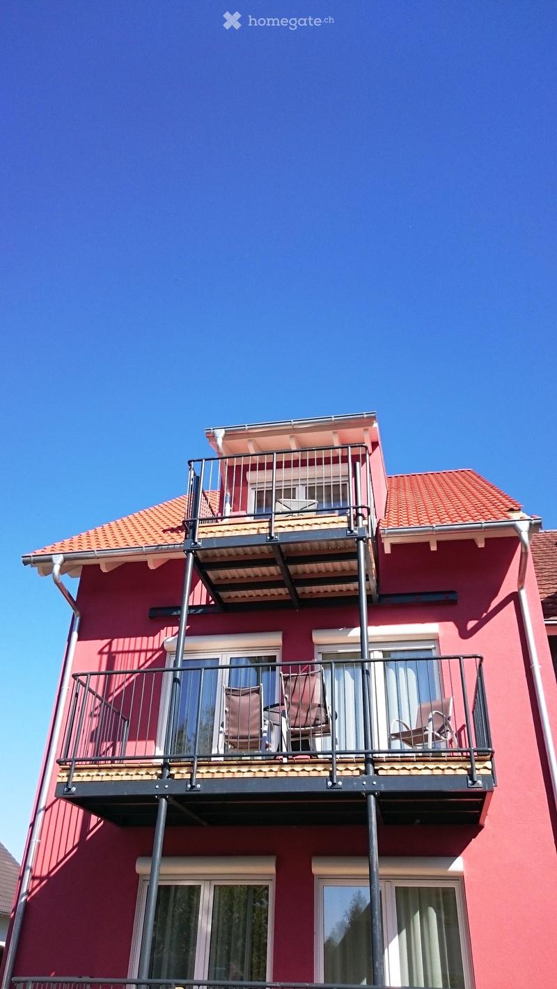 Two-story building with red brick exterior, multiple balconies with metal railings, and tiled roofs.