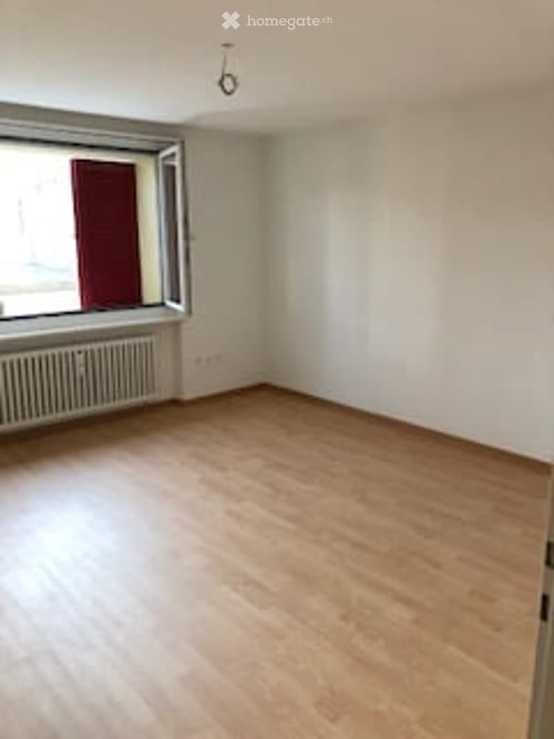 Empty room with wooden flooring, white walls, and a large window with a radiator below it.