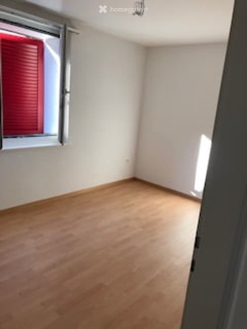 Empty room with wooden flooring, white walls, and two windows with blinds.