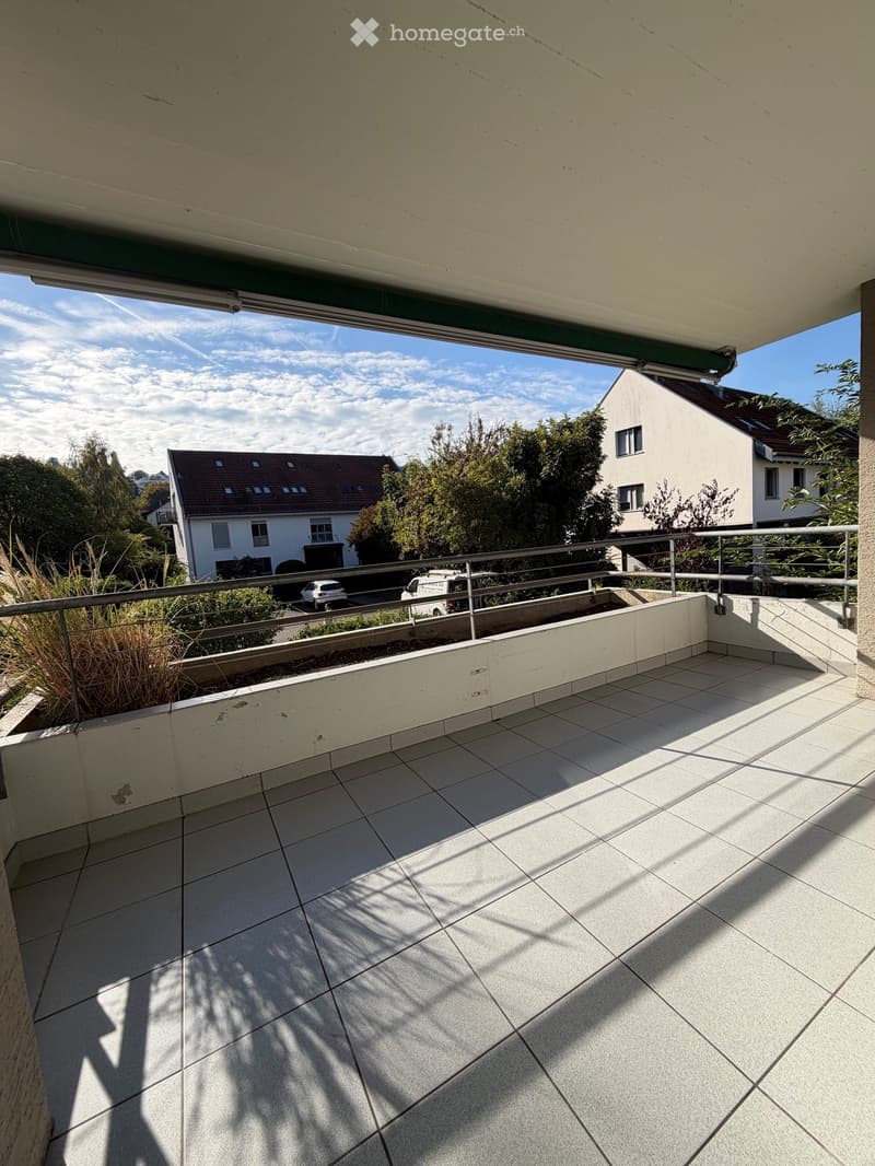 Balcony with tiled floor, metal railing, and view of neighboring houses and trees.