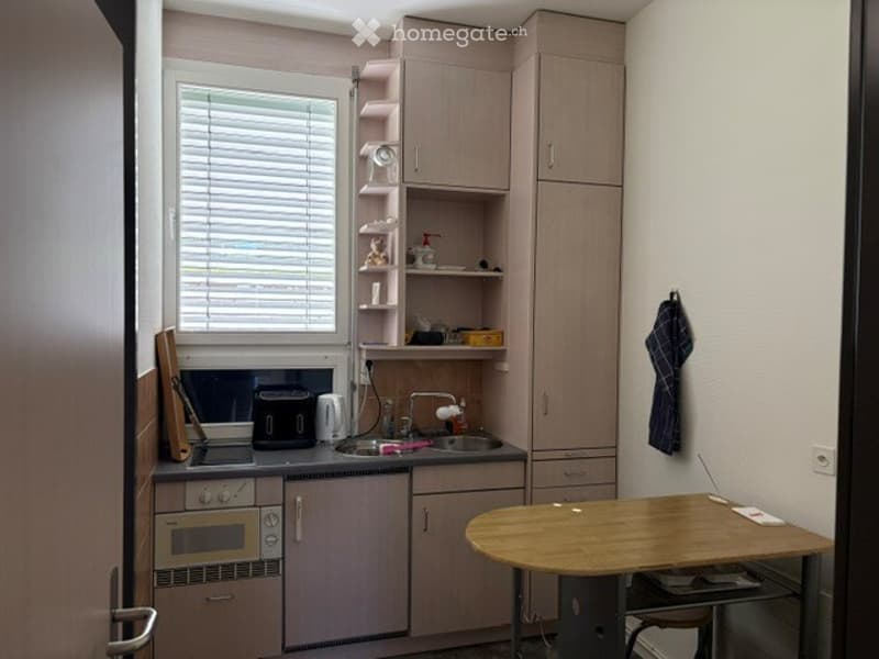 Compact kitchen with light wood cabinets, a small table, and essential appliances including an oven, microwave, and sink.