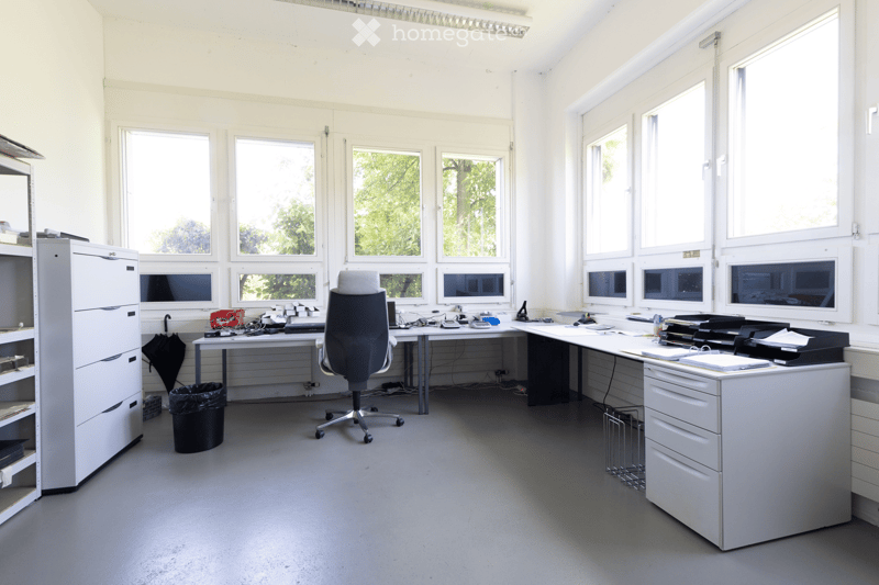 Office space with large windows, desks, chairs, filing cabinets, and office equipment.