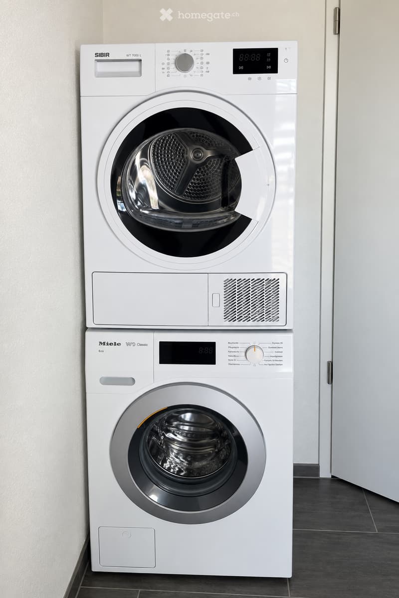 Two stacked white washing machine and dryer units with digital displays and control panels, placed against a light-colored wall.