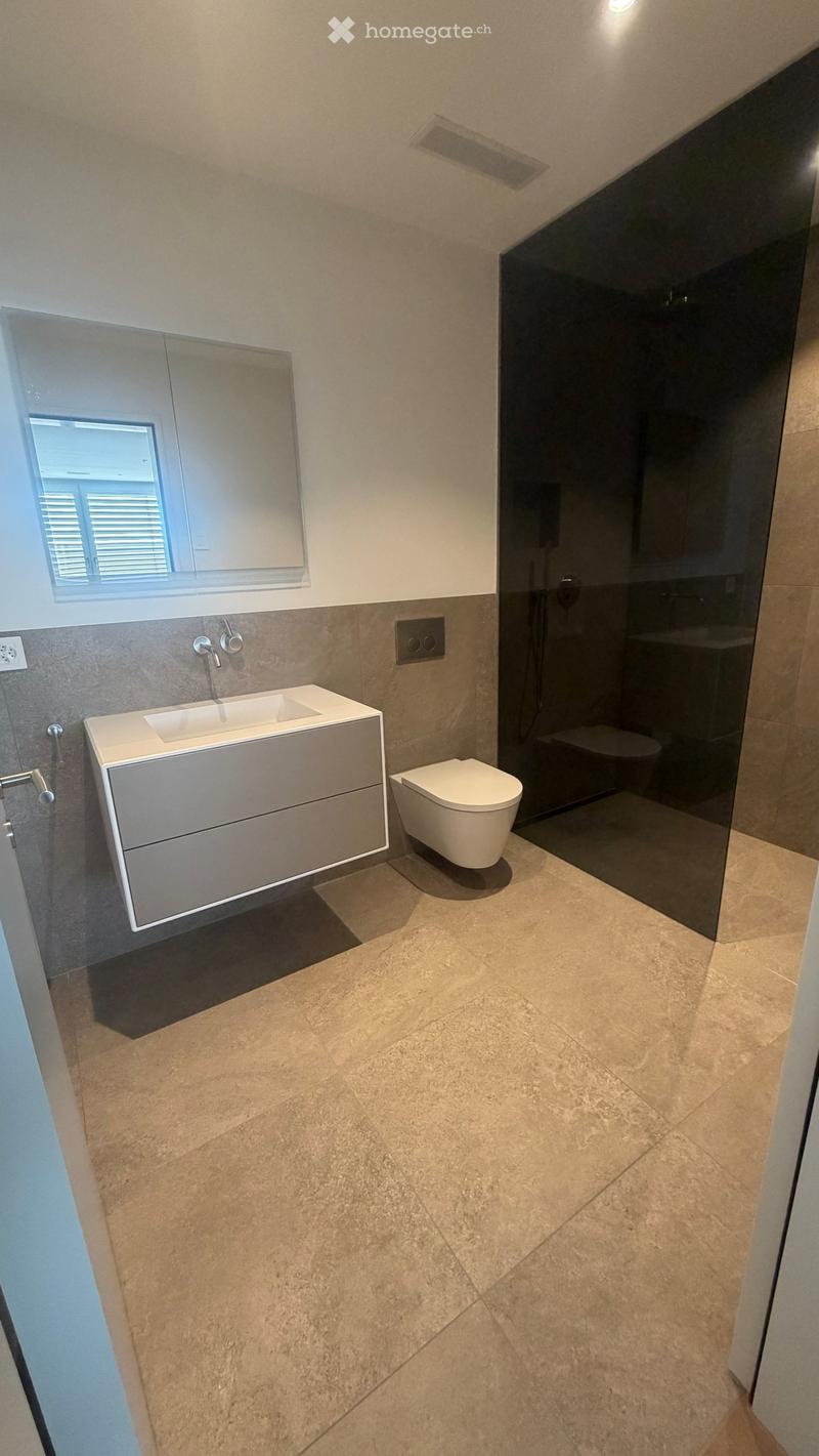 Modern bathroom with a white sink, toilet, mirrored cabinet, and large window. Features beige tiled flooring and grey walls.