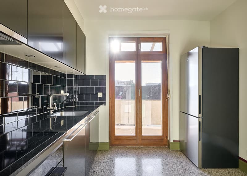 Modern kitchen with dark tiled backsplash, stainless steel appliances, and a large windowed door leading outside.