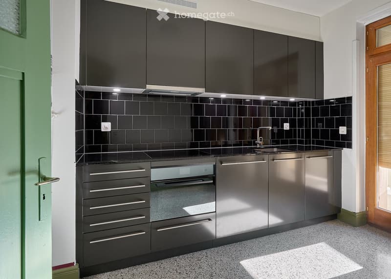 Modern kitchen with black tiled backsplash, stainless steel appliances, and sleek cabinetry.
