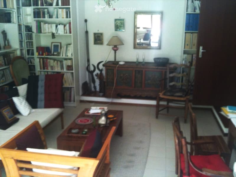 A cozy living room with a sofa, coffee table, chairs, bookshelf, table lamp, and a mirror. The room features a mix of wooden and upholstered furniture, creating a warm and inviting atmosphere.