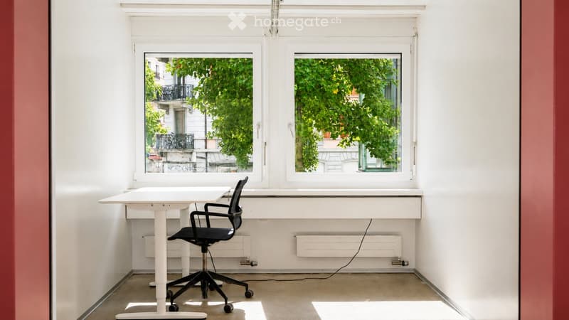 Bright, minimalist room with white walls, large windows, a white desk, and a black office chair.