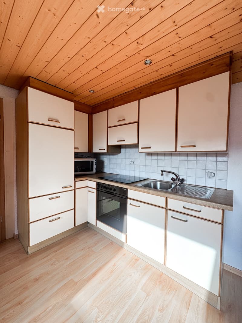 Modern kitchen with light-colored cabinets, wooden flooring, and stainless steel appliances including an oven, microwave, and sink.