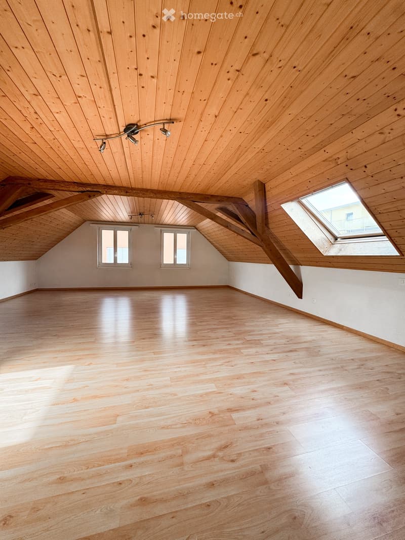Empty attic space with wooden floors and exposed wooden beams, featuring skylight windows and recessed lighting fixtures.