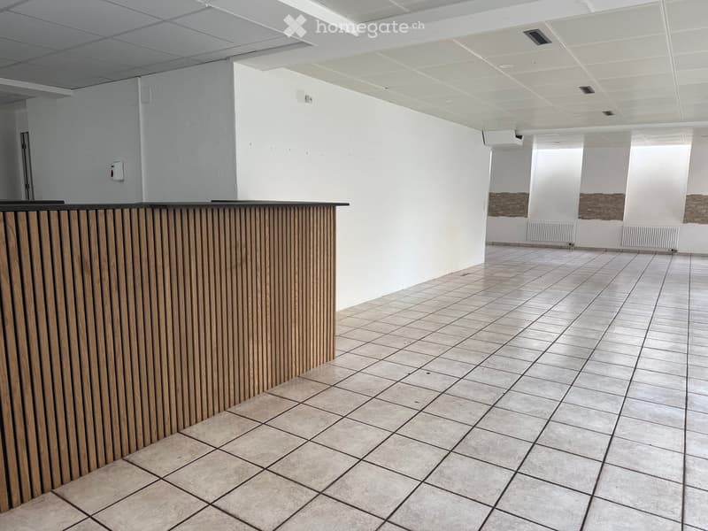 Empty room with white walls, tiled floor, and a wooden reception desk on the left side.