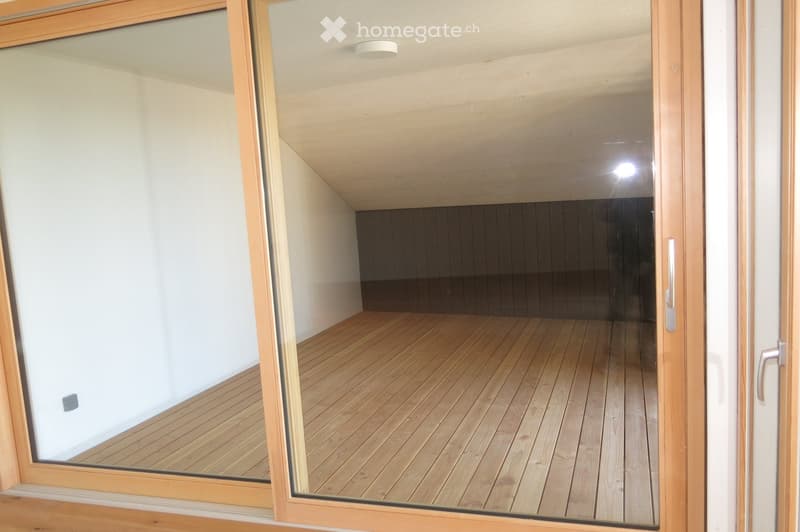 Empty room with wooden flooring and white walls, viewed through a glass door with wooden frame.