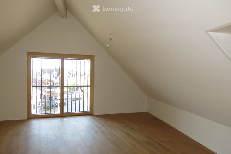 Empty attic room with wooden flooring, large skylight window, and sliding glass door leading to a balcony.