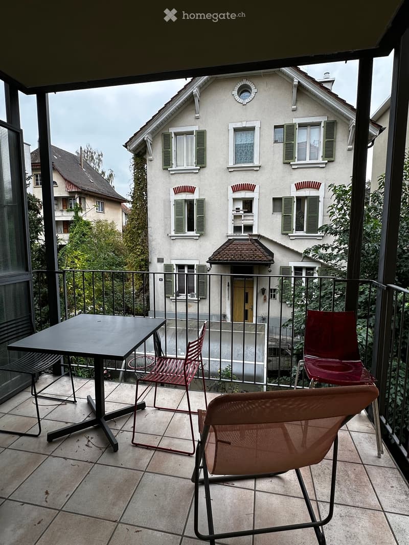 Balcony with tiled floor, black metal railing, and outdoor furniture including a black table and red and brown chairs.