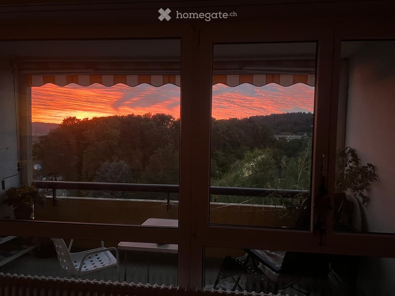 Balcony with a scenic sunset view, featuring a white plastic chair and a small table.