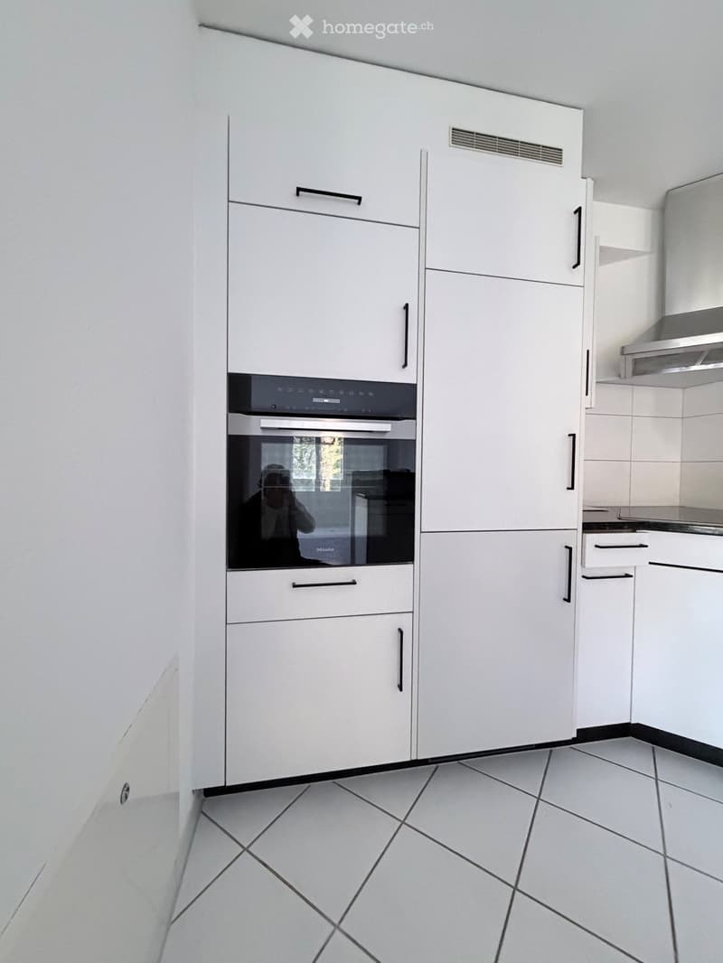 Modern kitchen with white cabinets, an integrated oven, and tiled flooring.