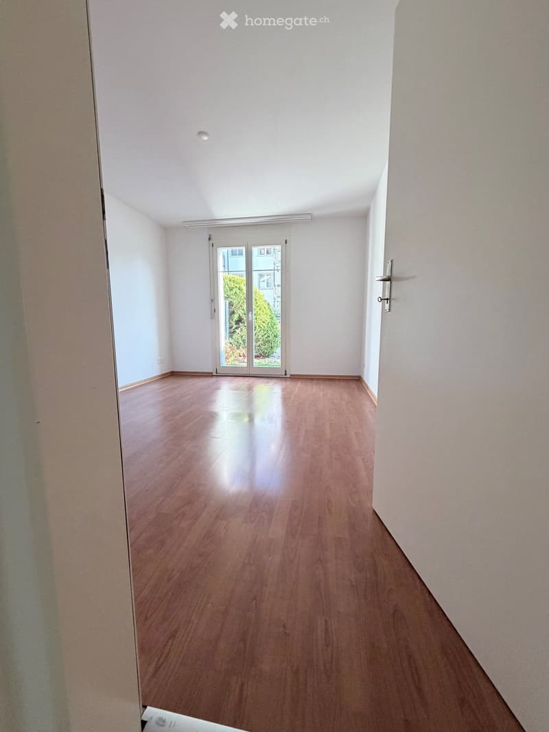 Empty hallway with wooden flooring, white walls, and a sliding glass door leading outside.