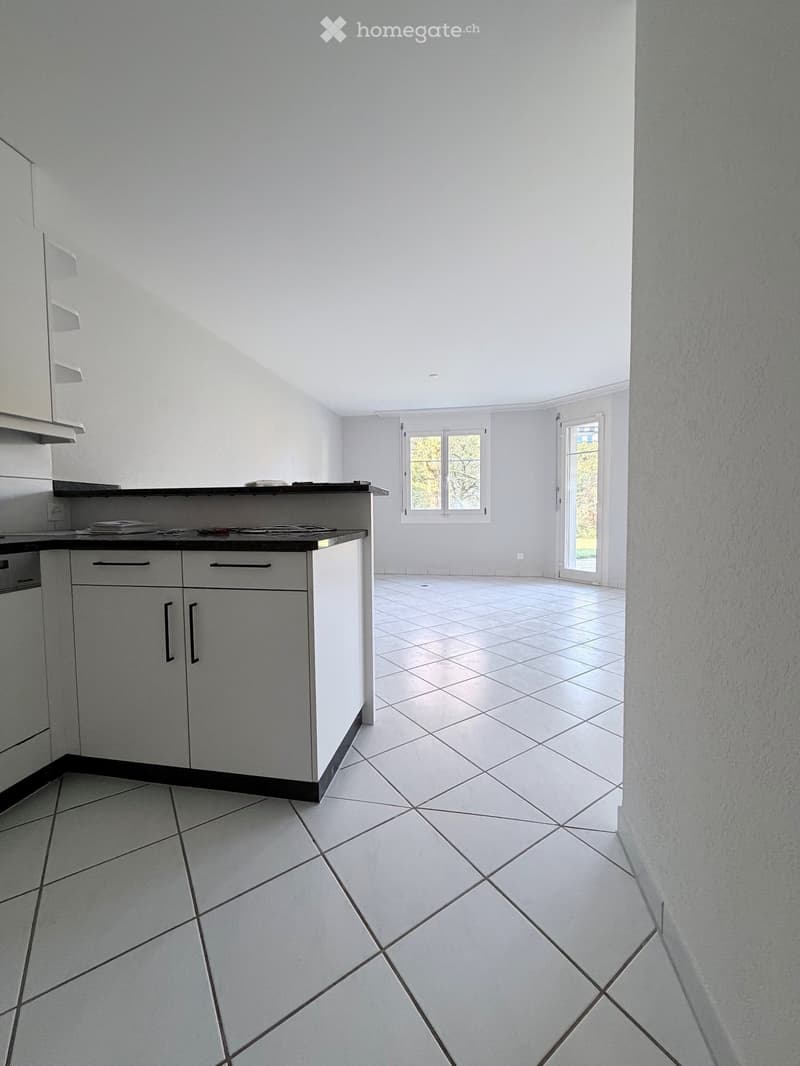 Empty kitchen with white tiled floor, white cabinets, and a black countertop. There are two windows and a door leading outside.